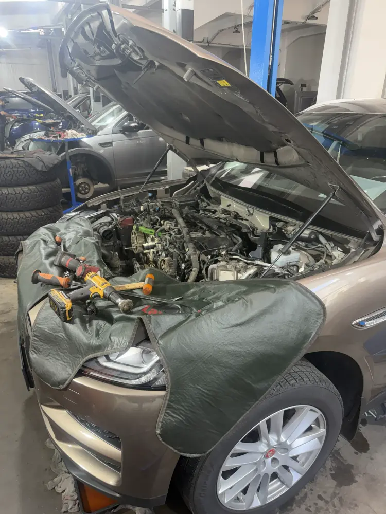 Jaguar F-Pace în atelier, cu capota ridicată și husele de protecție montate